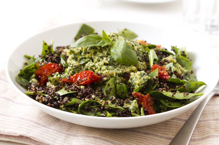 a salad with greens, sundried tomatoes, quinoa in a white bowl